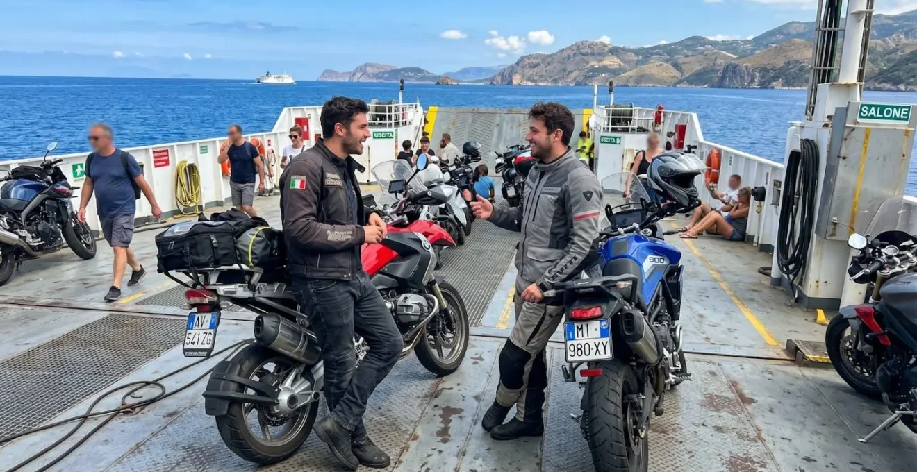 Due motociclisti in conversazione sul ponte di una nave traghetto, con il mare sullo sfondo
